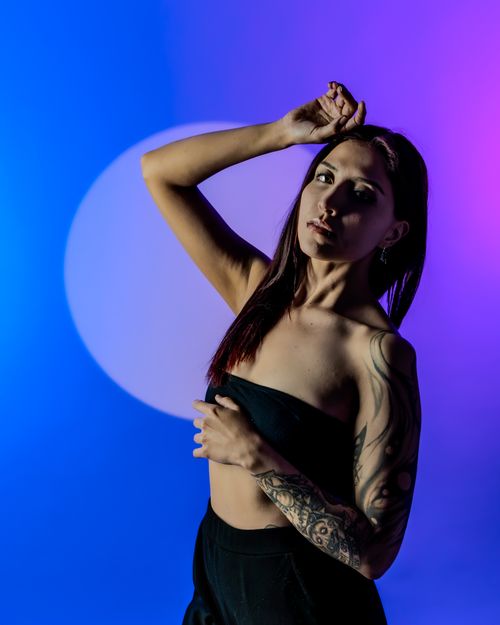 Free Portrait of a woman posing in colorful studio lighting with tattoos and elegant style. Stock Photo
