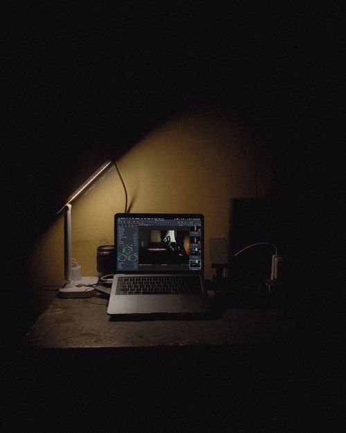 Free Dimly lit workstation featuring a laptop and desk lamp in an artistic setup. Stock Photo