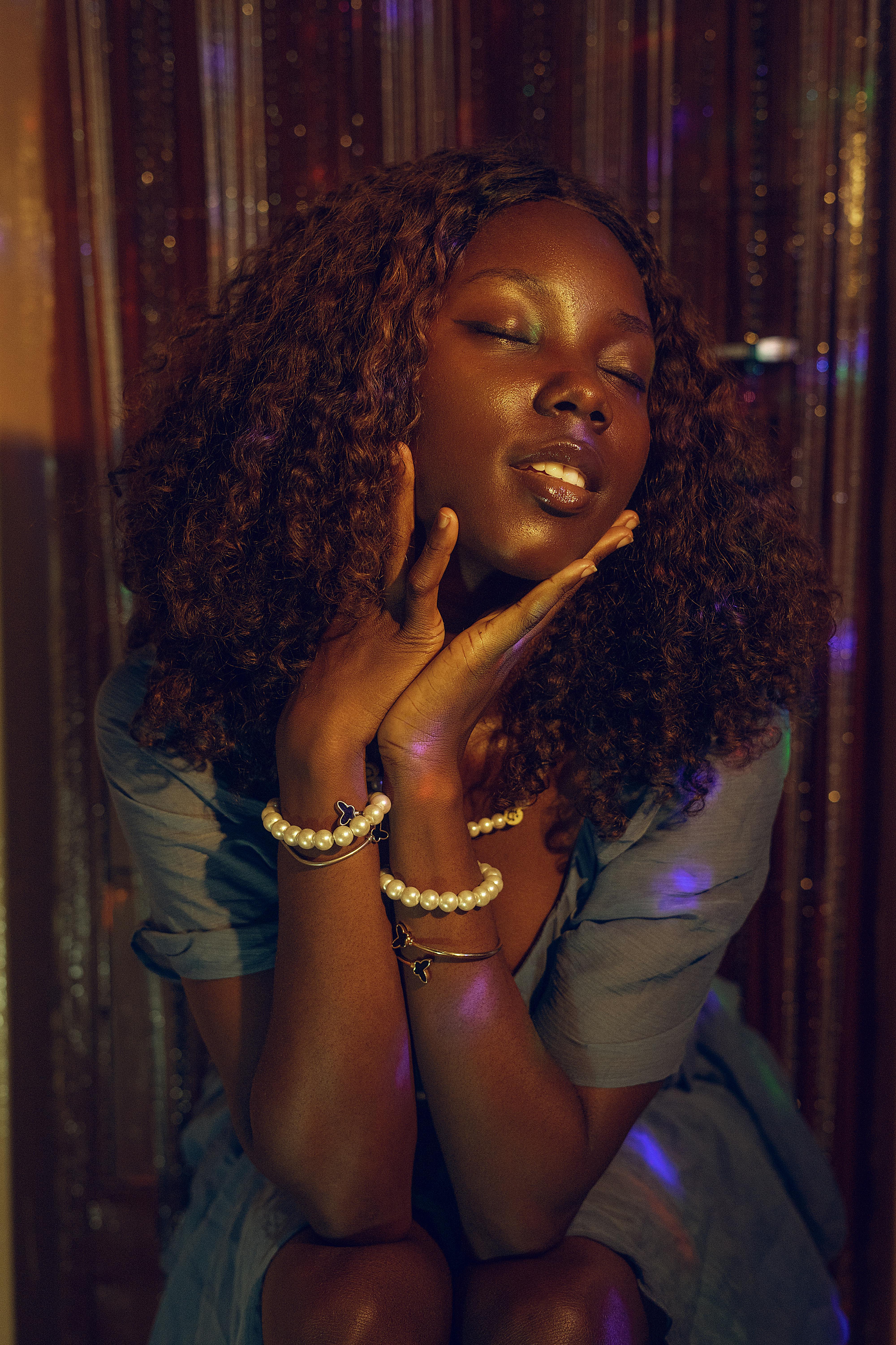Stylish portrait of a woman with pearls and expressive pose under ambient lighting.