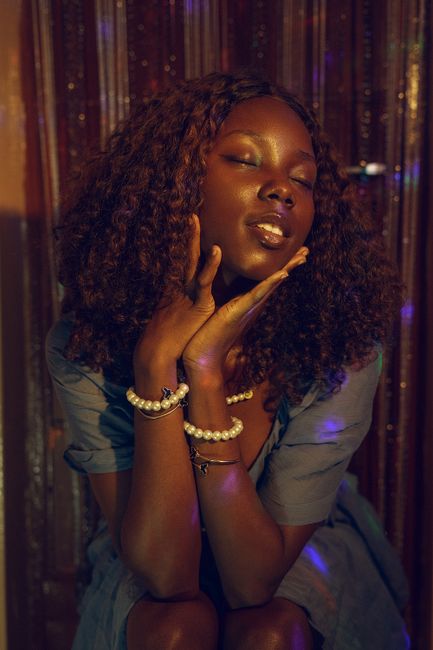 Stylish portrait of a woman with pearls and expressive pose under ambient lighting.