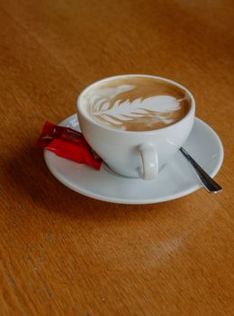 Enjoy a beautifully crafted latte art coffee with biscuit on a cozy wooden table setting.
