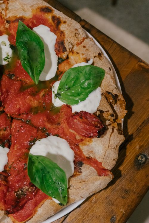 Free Close-up of a Margherita pizza topped with fresh basil and mozzarella on a rustic wooden table. Stock Photo