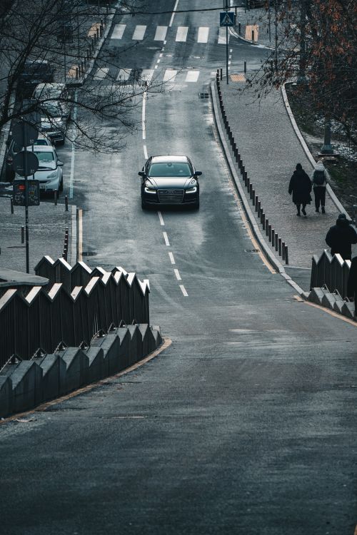 Free A black car driving on a quiet road with pedestrians in Kyiv, Ukraine, during a crisp day. Stock Photo