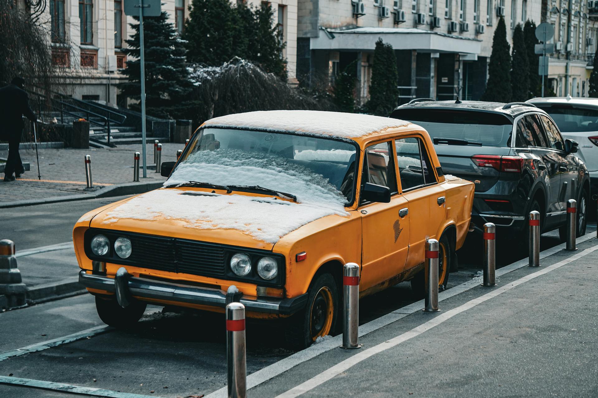 A vintage yellow car covered in snow parked on a street in Kyiv, Ukraine.