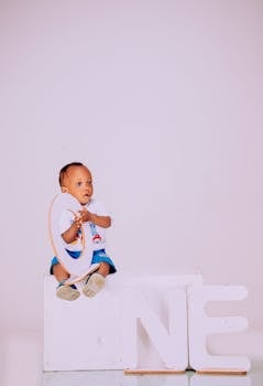 Sweet baby sitting with birthday decoration spelling 'ONE'.