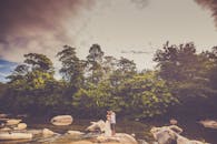 一对夫妇站在宁静河边的岩石上，深情地望向四周，周围树木茂密