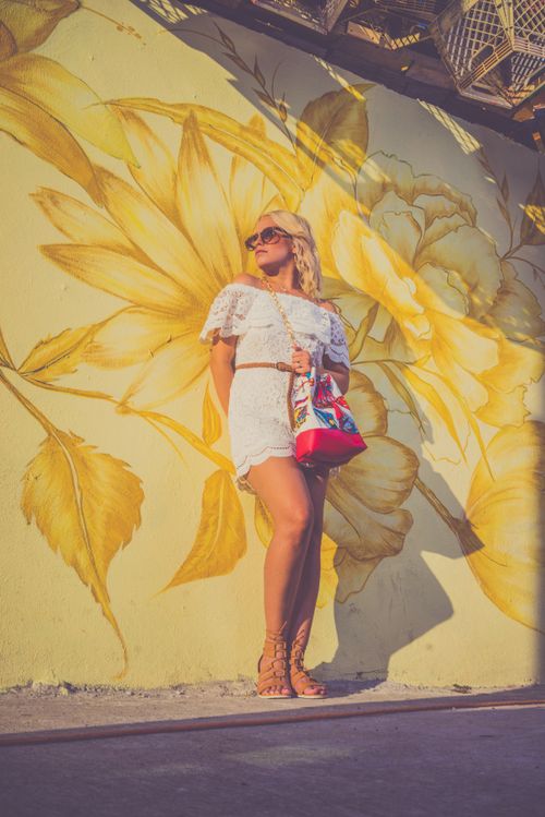Free Fashionable woman in white dress poses confidently against a yellow floral mural outdoors. Stock Photo