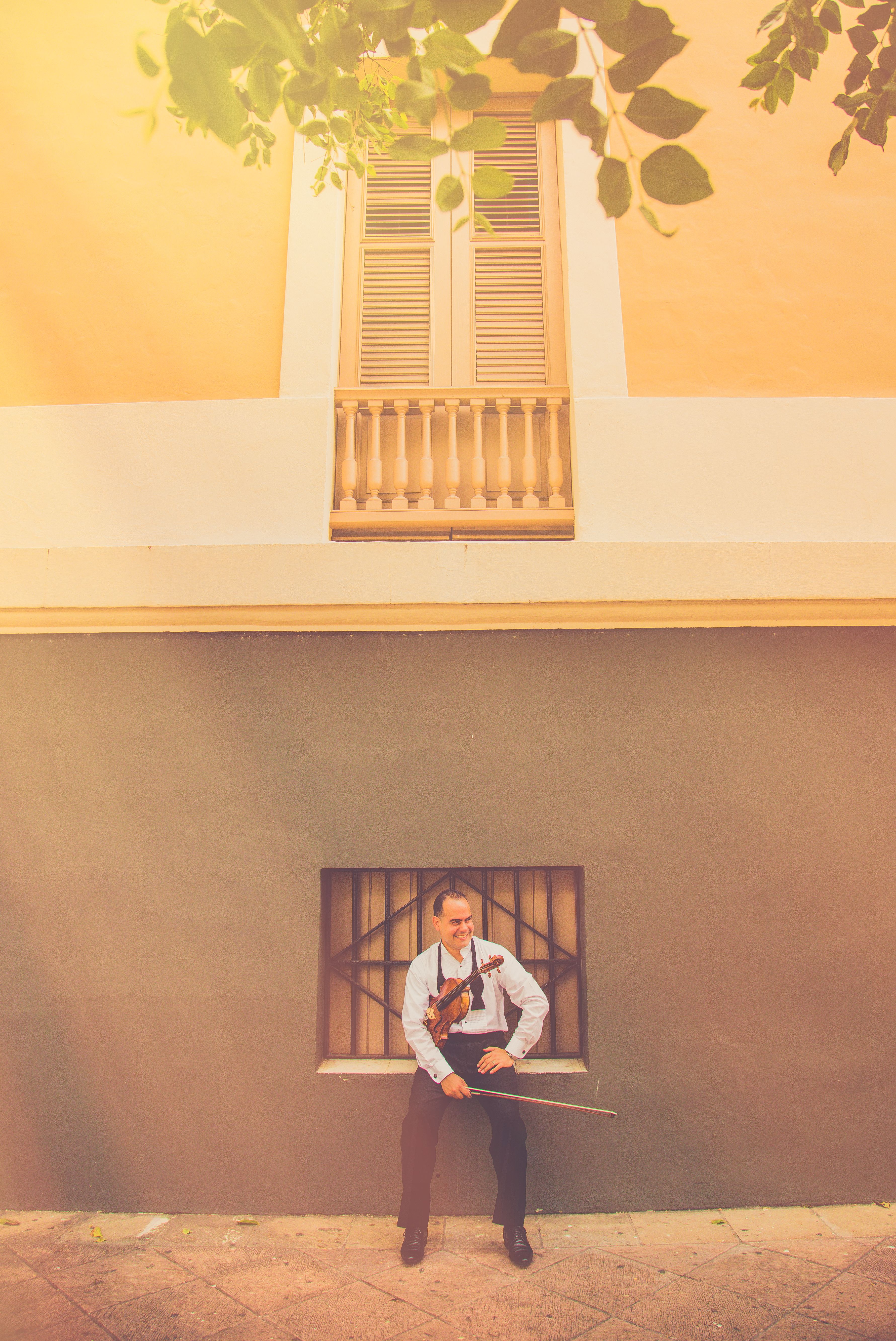 A serene moment of a violinist sitting outdoors against a sunlit wall, holding a violin.
