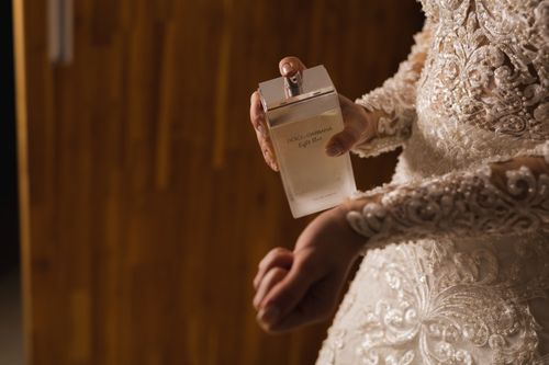 Free Bride in lace gown holding Dolce & Gabbana perfume, expressing elegance. Stock Photo