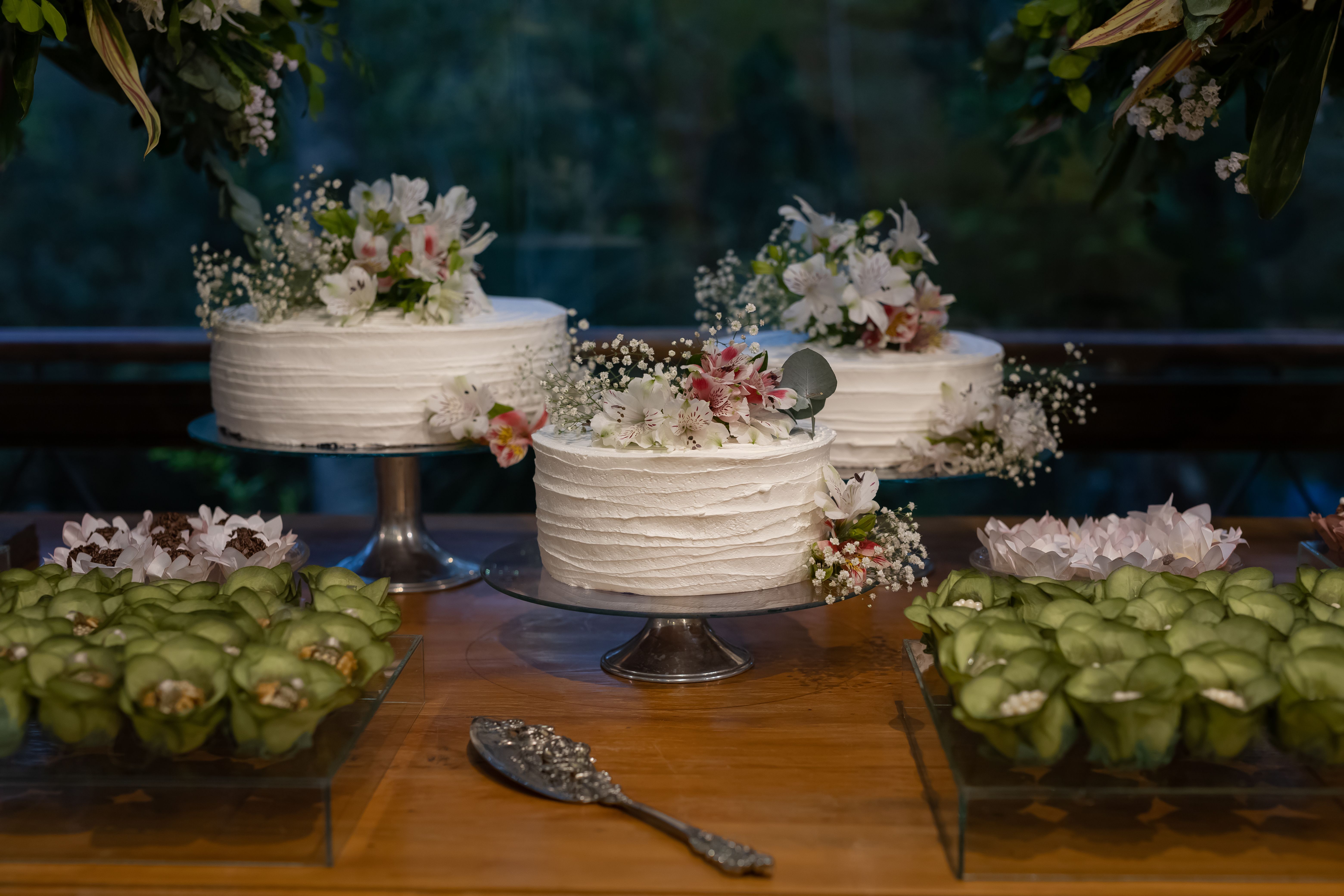 Three beautifully decorated white cakes with floral arrangements showcased on a dessert table.
