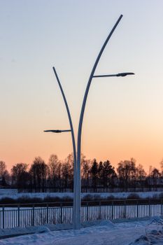 Elegant street lamps against a winter sunset with snow-covered ground.