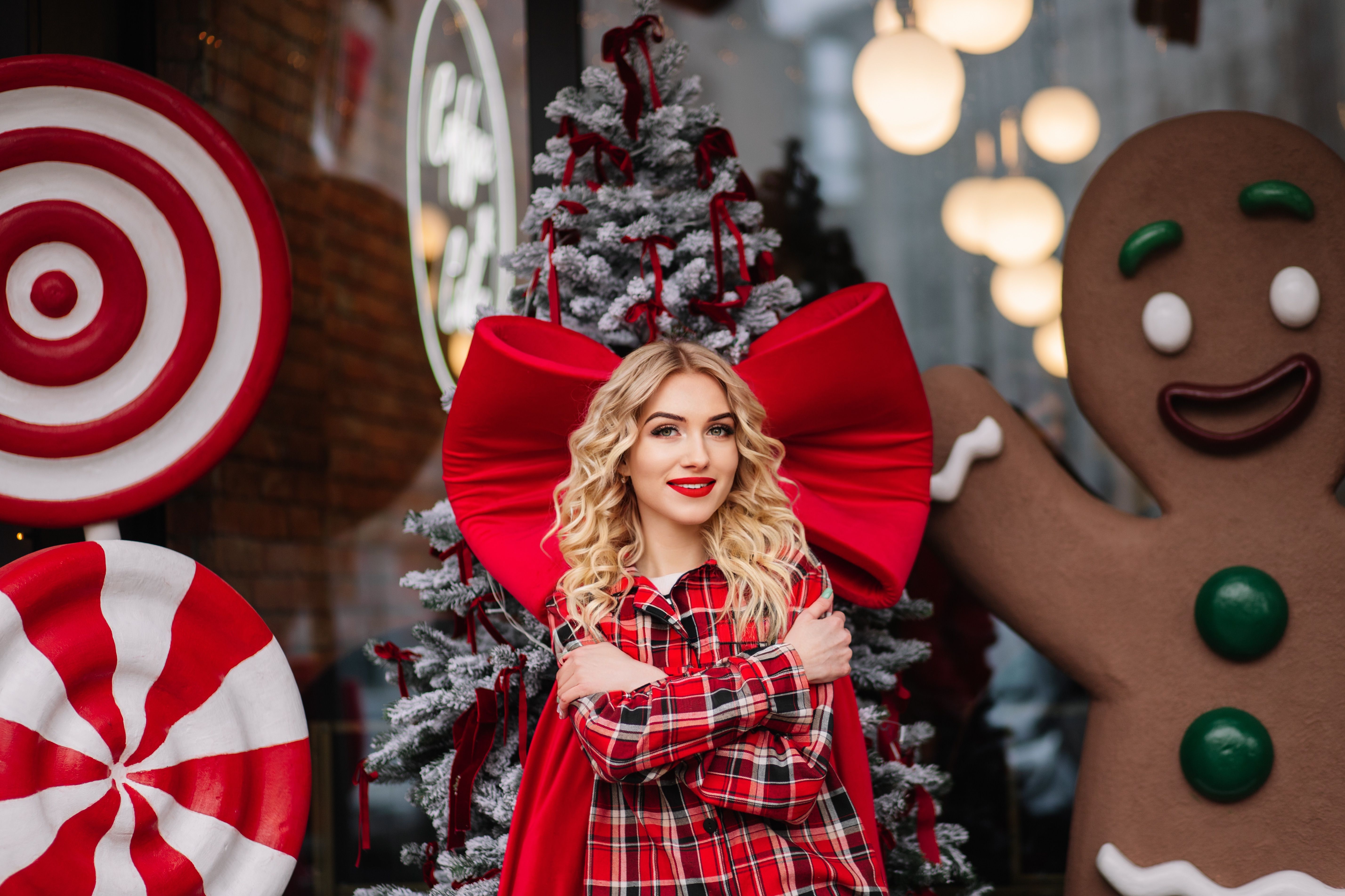 A cheerful woman posing with giant candy decorations and a Christmas tree, embracing the holiday spirit.