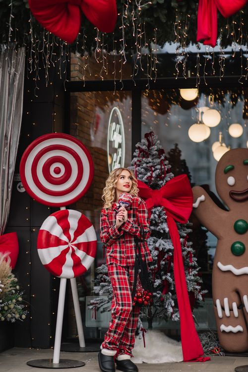Free Woman in festive pajamas standing in a holiday decorated outdoor scene with candy and lights. Stock Photo