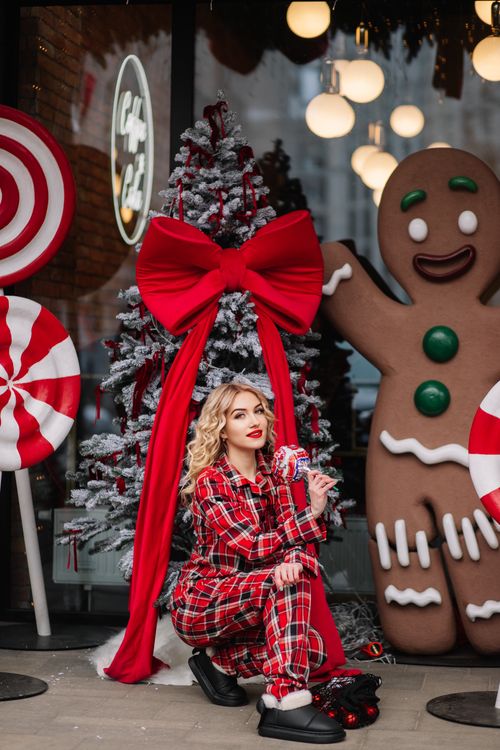 Free Woman in plaid pajamas by Christmas decorations. Gingerbread and candy cane theme with festive tree. Stock Photo