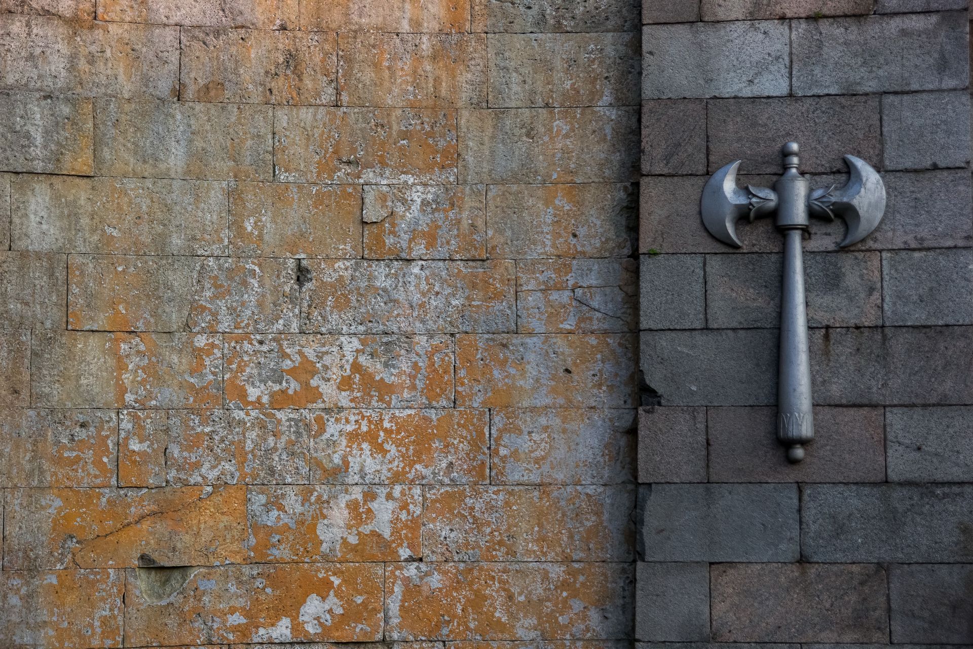 Worn stone wall with a decorative double-headed axe mounted on it.