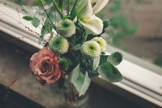 A beautiful floral arrangement featuring roses and chrysanthemums by a window.