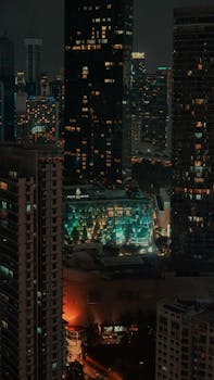 A vibrant aerial view of Kuala Lumpur's cityscape at night, featuring modern architecture and luminous city lights.
