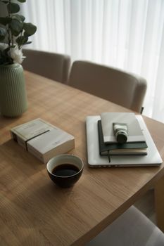 A cozy home office setup with coffee, books, and greenery on a wooden table.