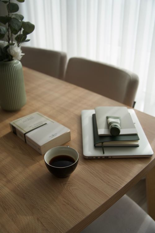 Free A cozy home office setup with coffee, books, and greenery on a wooden table. Stock Photo
