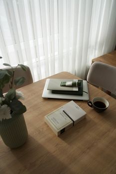Serene atmosphere with laptop, books, and coffee on a wooden table near window.