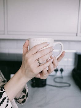 Hands holding a warm mug in a kitchen setting, invoking a calm morning vibe.