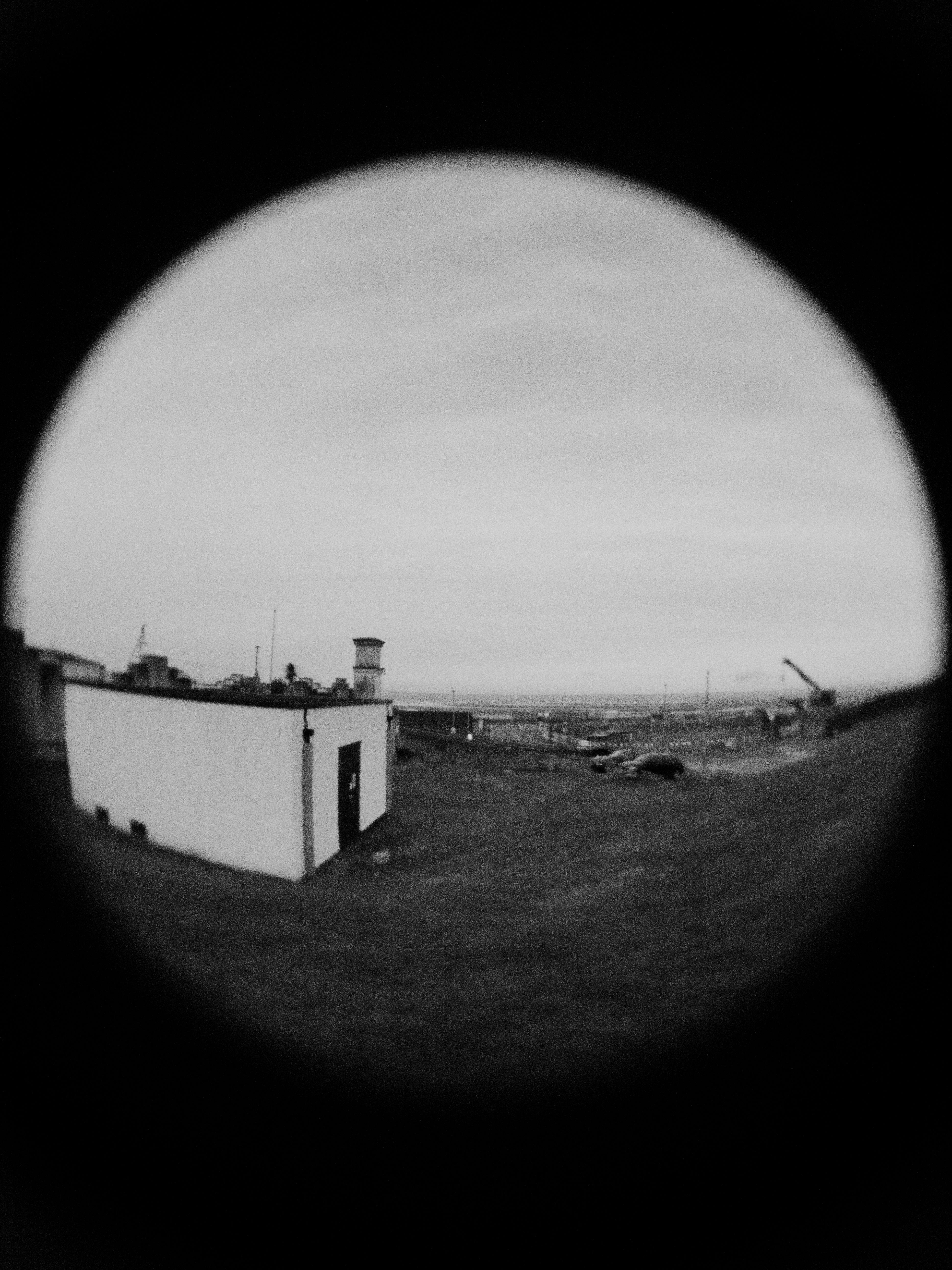 A fisheye view of a landscape captured in black and white, featuring a small building.