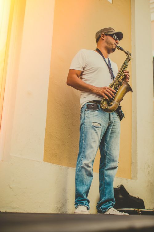Free Man playing saxophone outdoors in casual attire, adding a musical vibe to the urban scene. Stock Photo