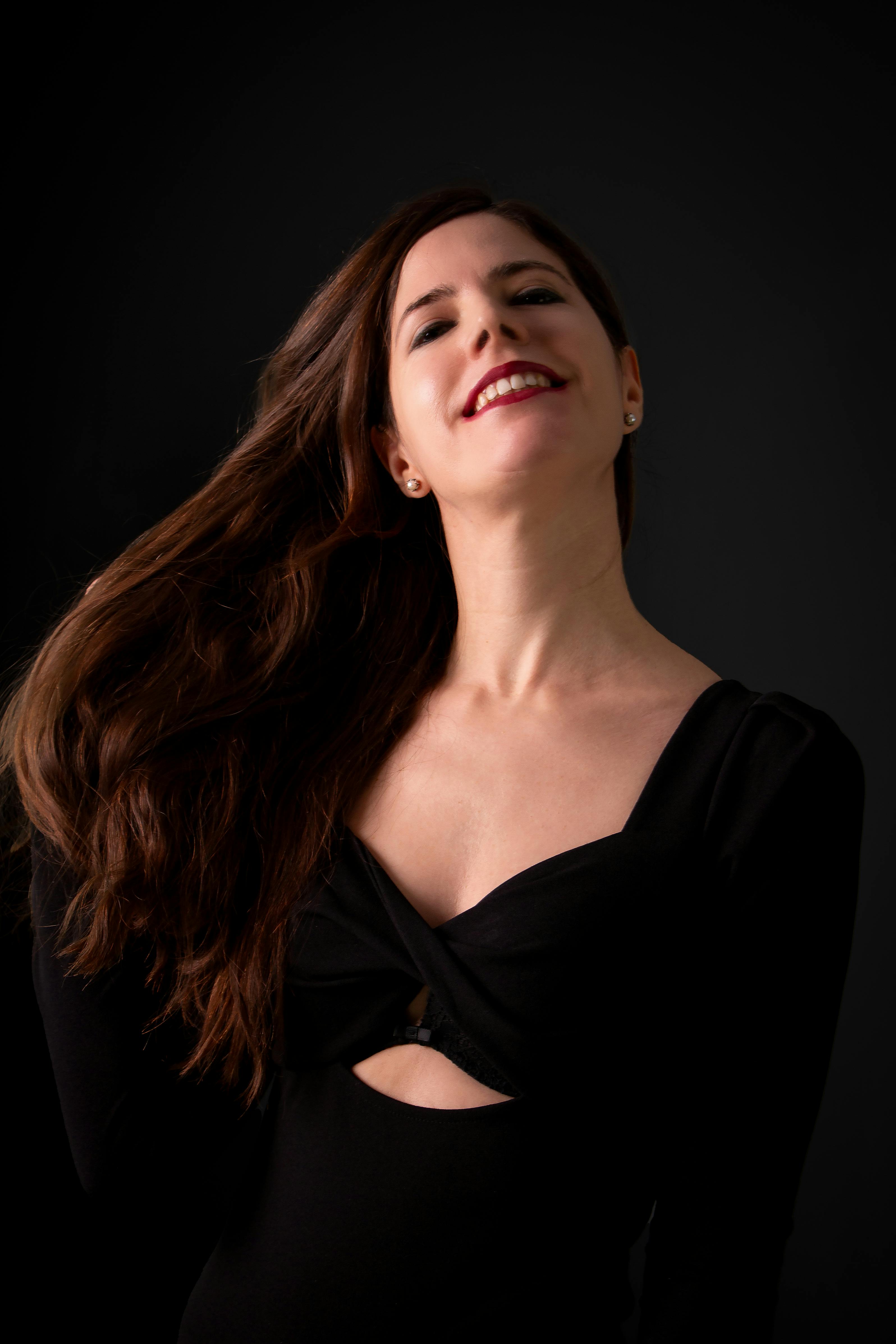 A charismatic woman with flowing hair and a radiant smile, captured against a dark background.