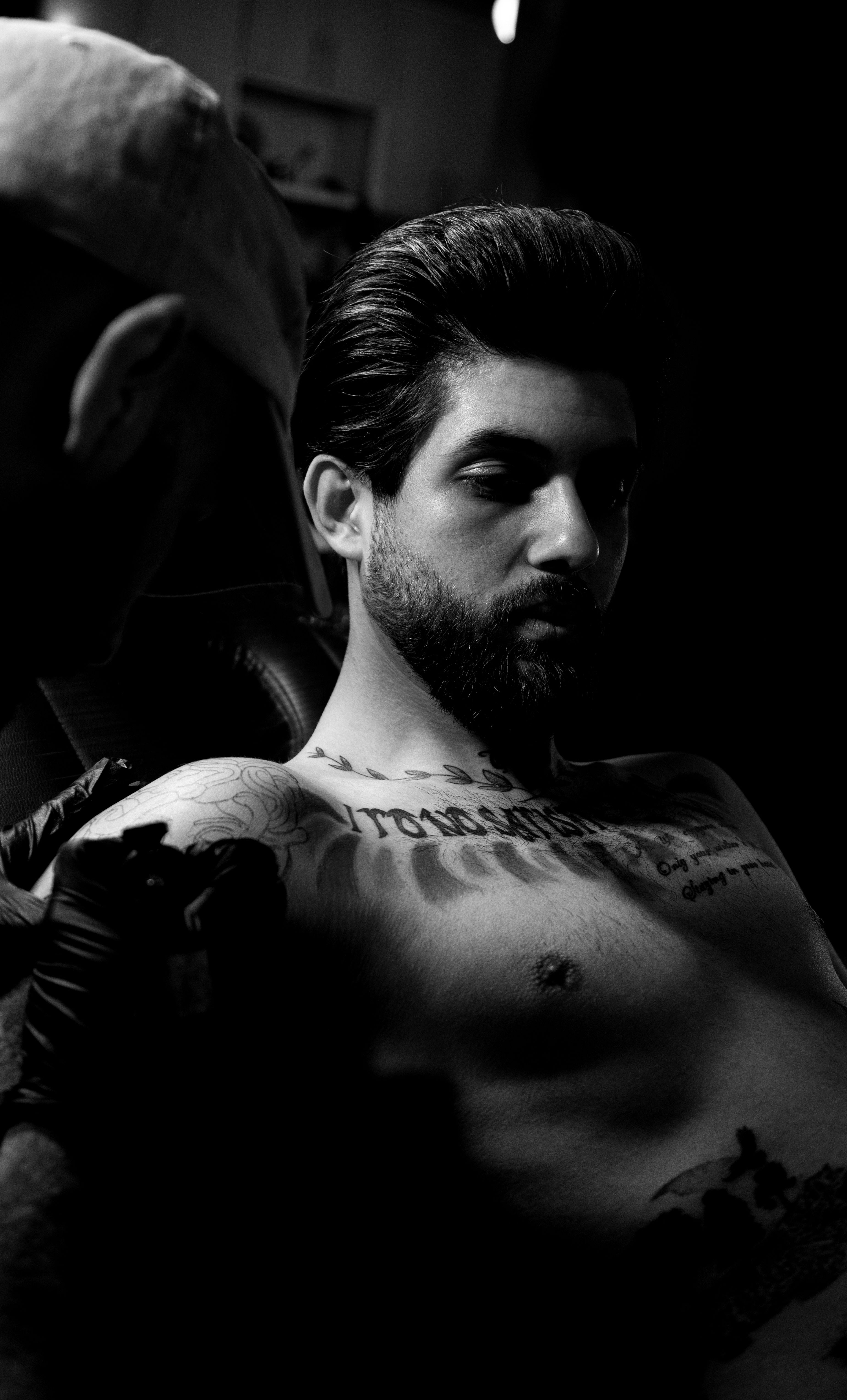 Striking black and white portrait capturing a man receiving a tattoo in dim lighting.