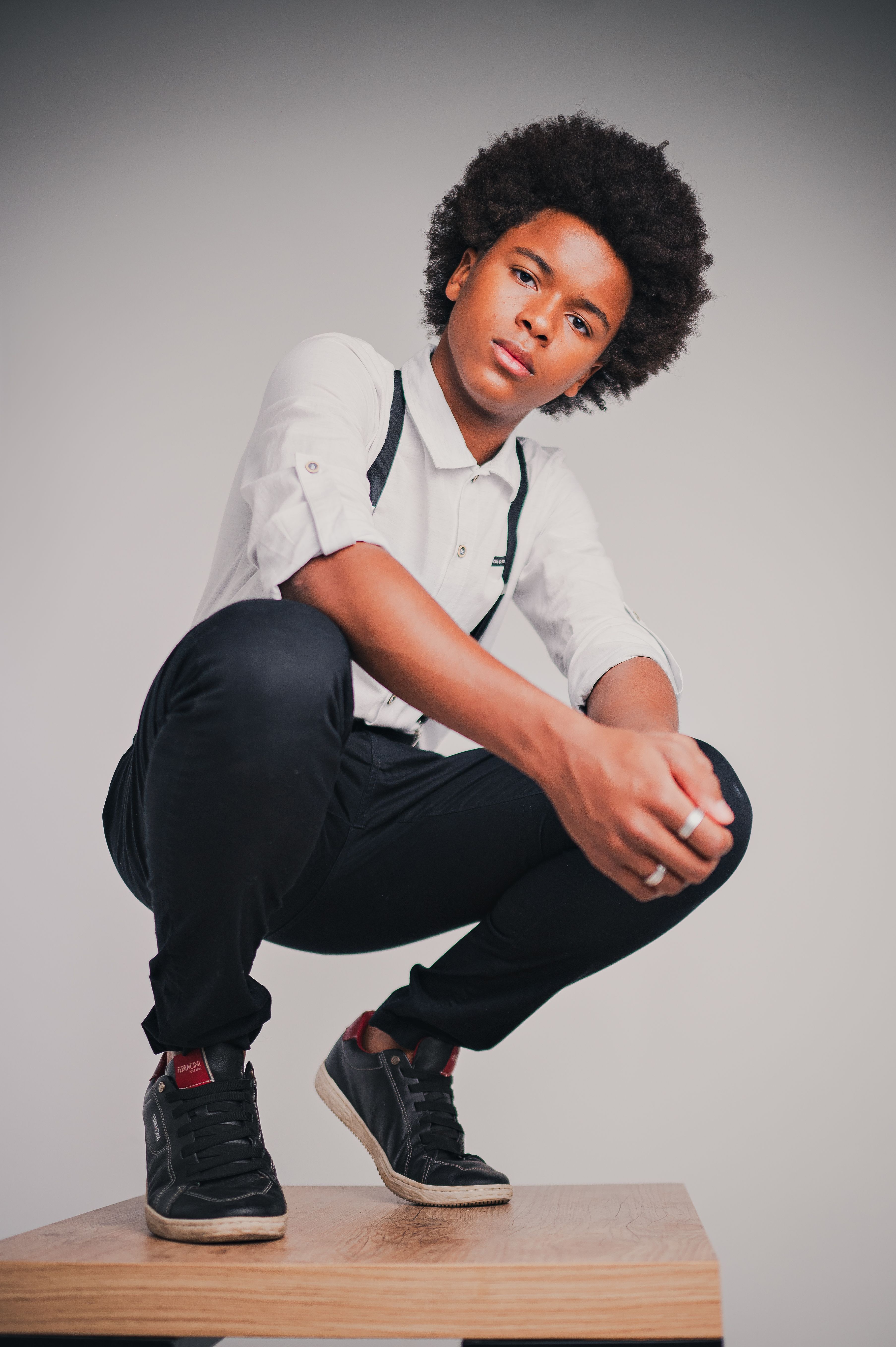 Portrait of a young adult with afro hair crouching indoors in a stylish outfit.