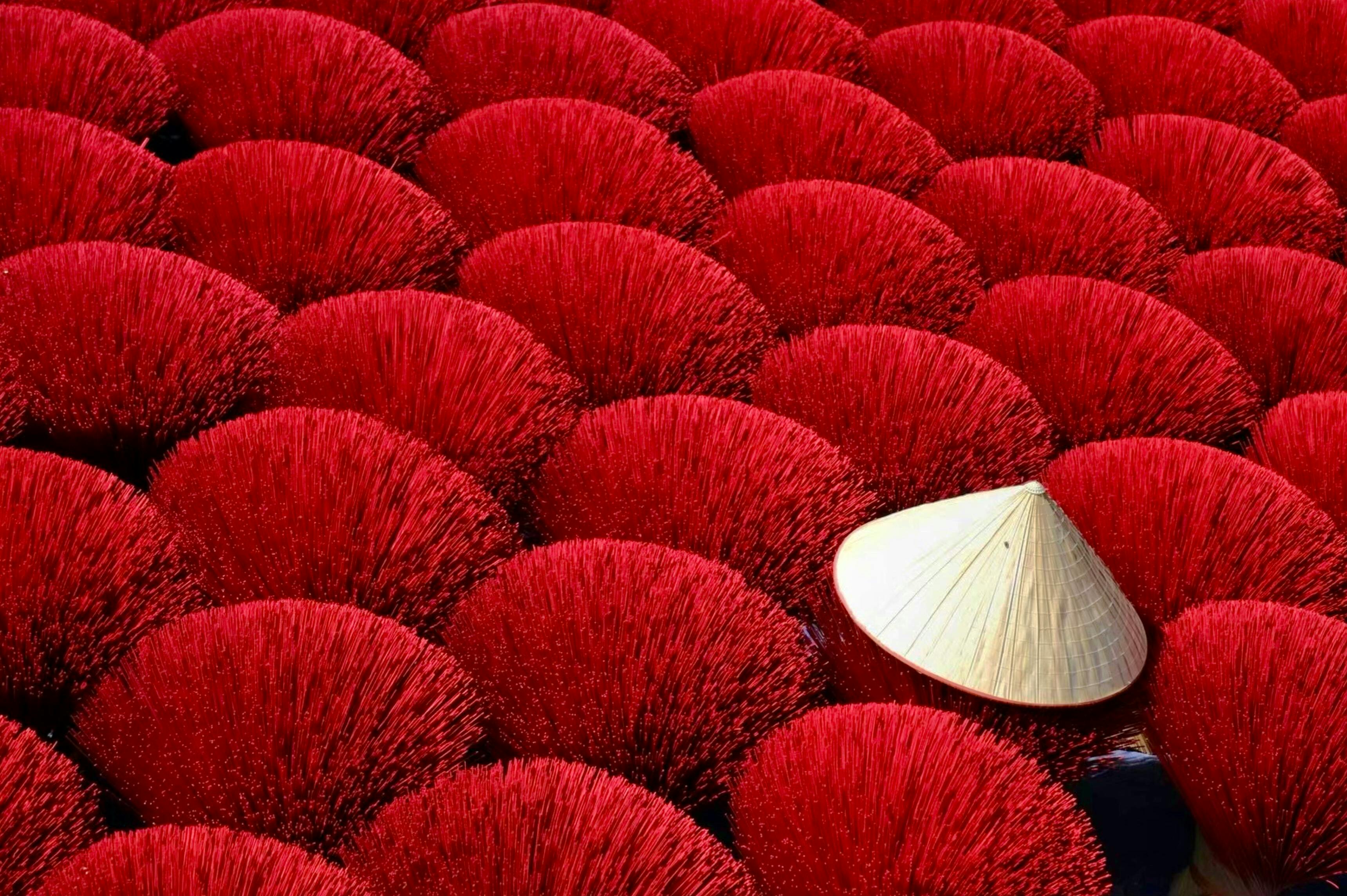 Bright red incense sticks drying in the sun with a conical hat adding cultural flair.