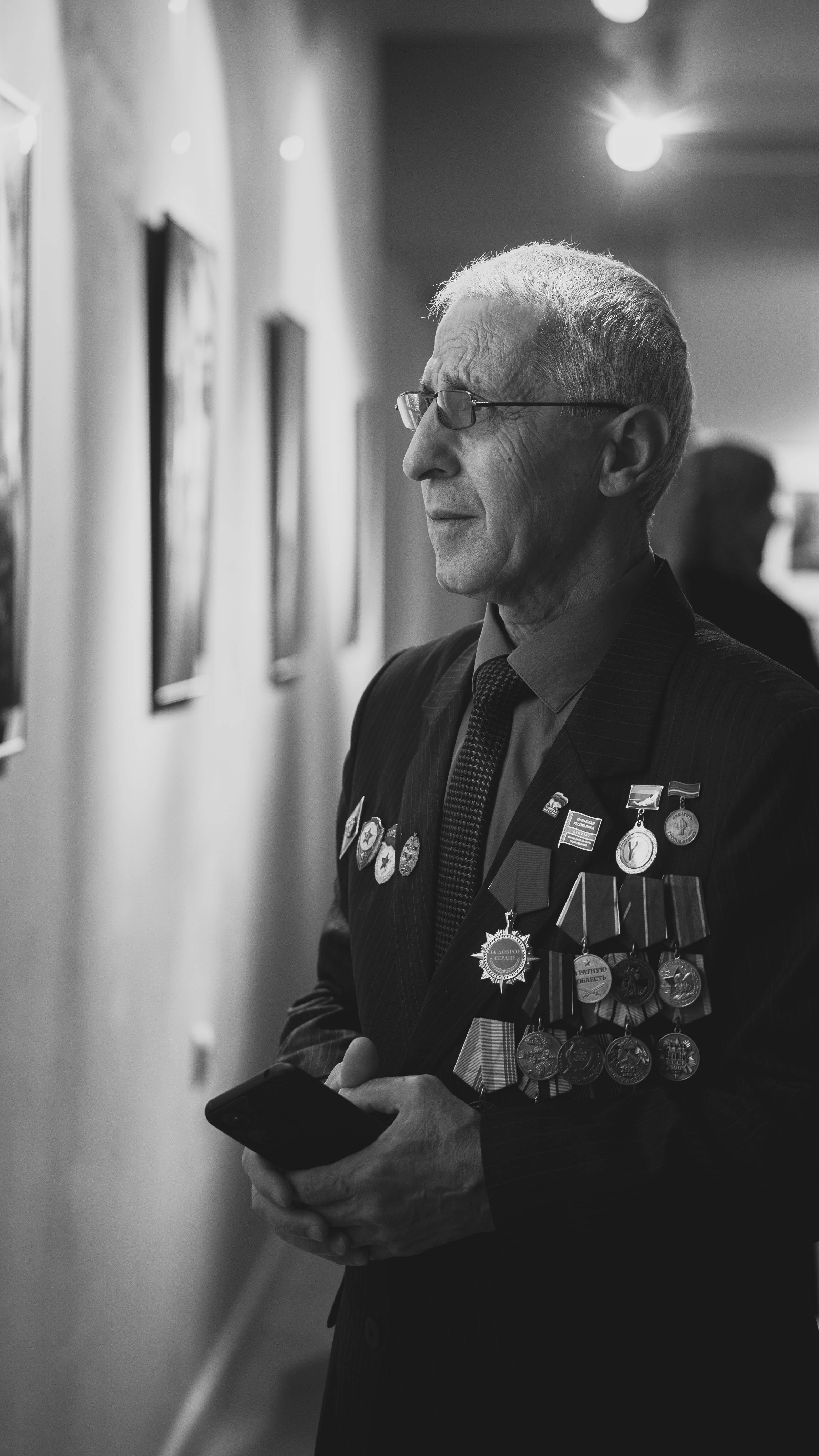 Black and white portrait of an elderly man with medals in an art gallery.