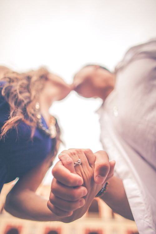 Free Romantic couple holding hands and kissing, focusing on the engagement ring and love expression. Stock Photo
