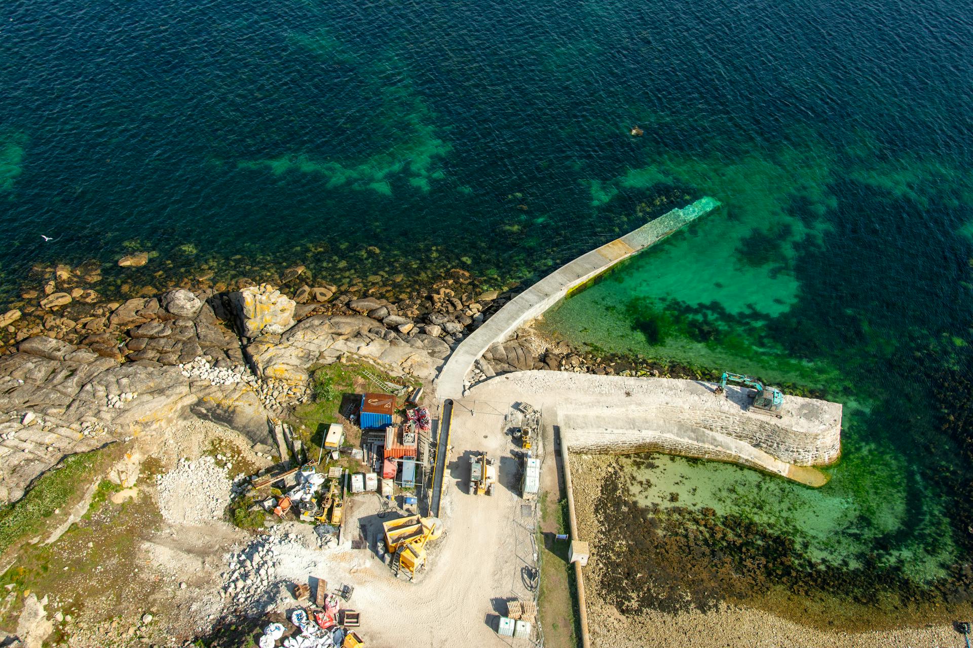 Aerial photo of a construction site on a coastal pier with clear turquoise waters.