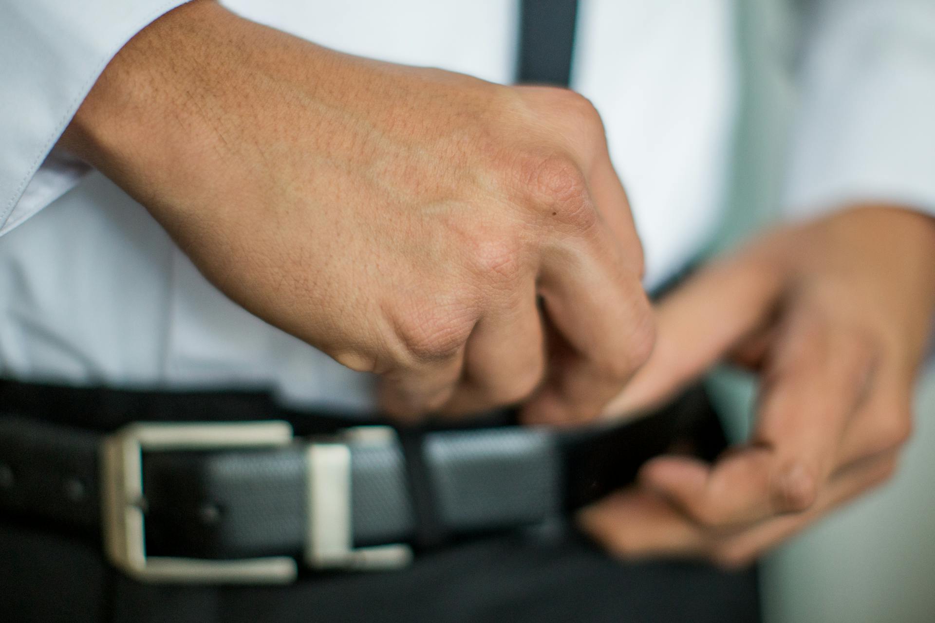 Close-up of a man adjusting his belt buckle, highlighting details of formal attire.