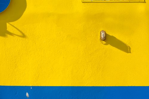 Free Bright yellow wall with a blue stripe and lamp casting a shadow, capturing minimalist design. Stock Photo