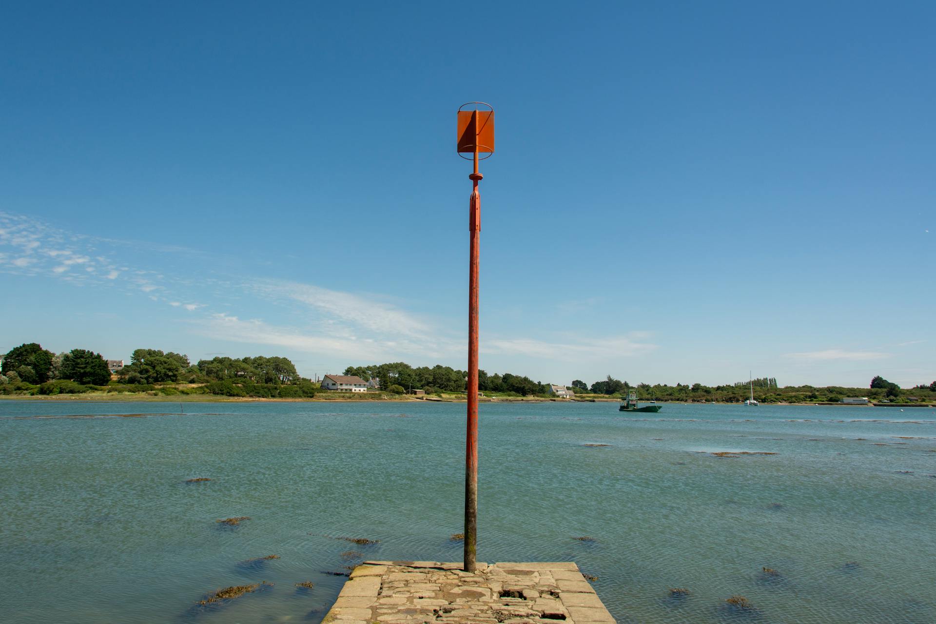 A solitary beacon post on a pier overlooking calm waters in Bretagne under a clear blue sky.