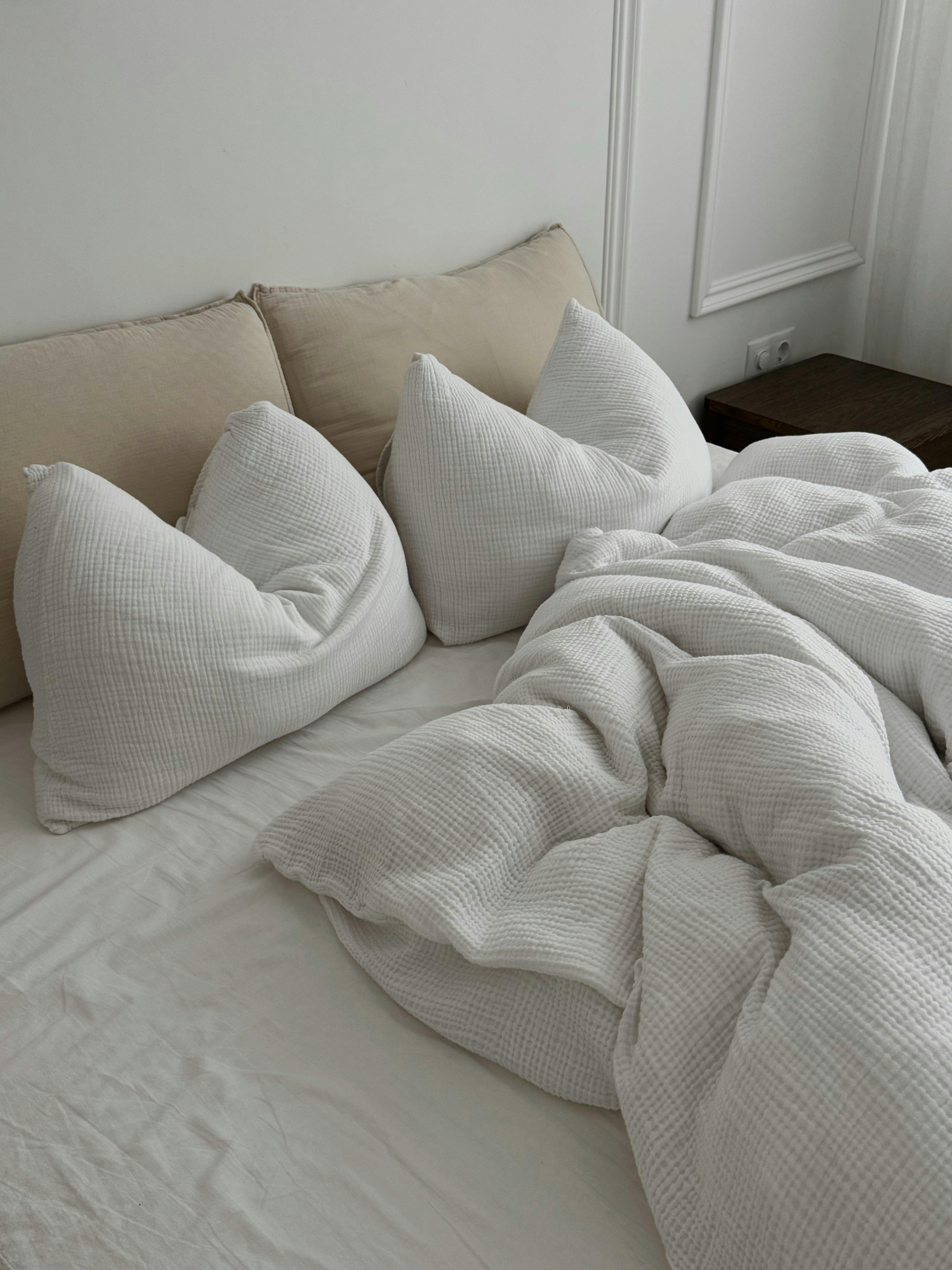 A minimalistic bedroom scene featuring a cozy, rumpled white bedding setup.