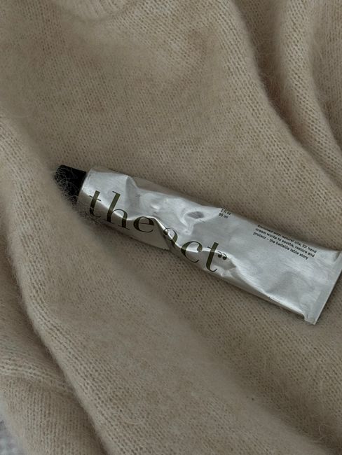 Minimalist shot of a crumpled cream tube on a textured beige blanket, highlighting cozy vibes.