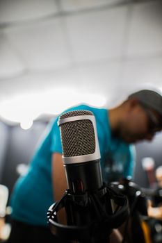 Focused shot of a condenser microphone in a recording studio with a person in the background.