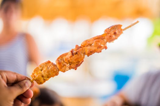 Close-up of a grilled chicken skewer held in a hand, blurred background adding depth.