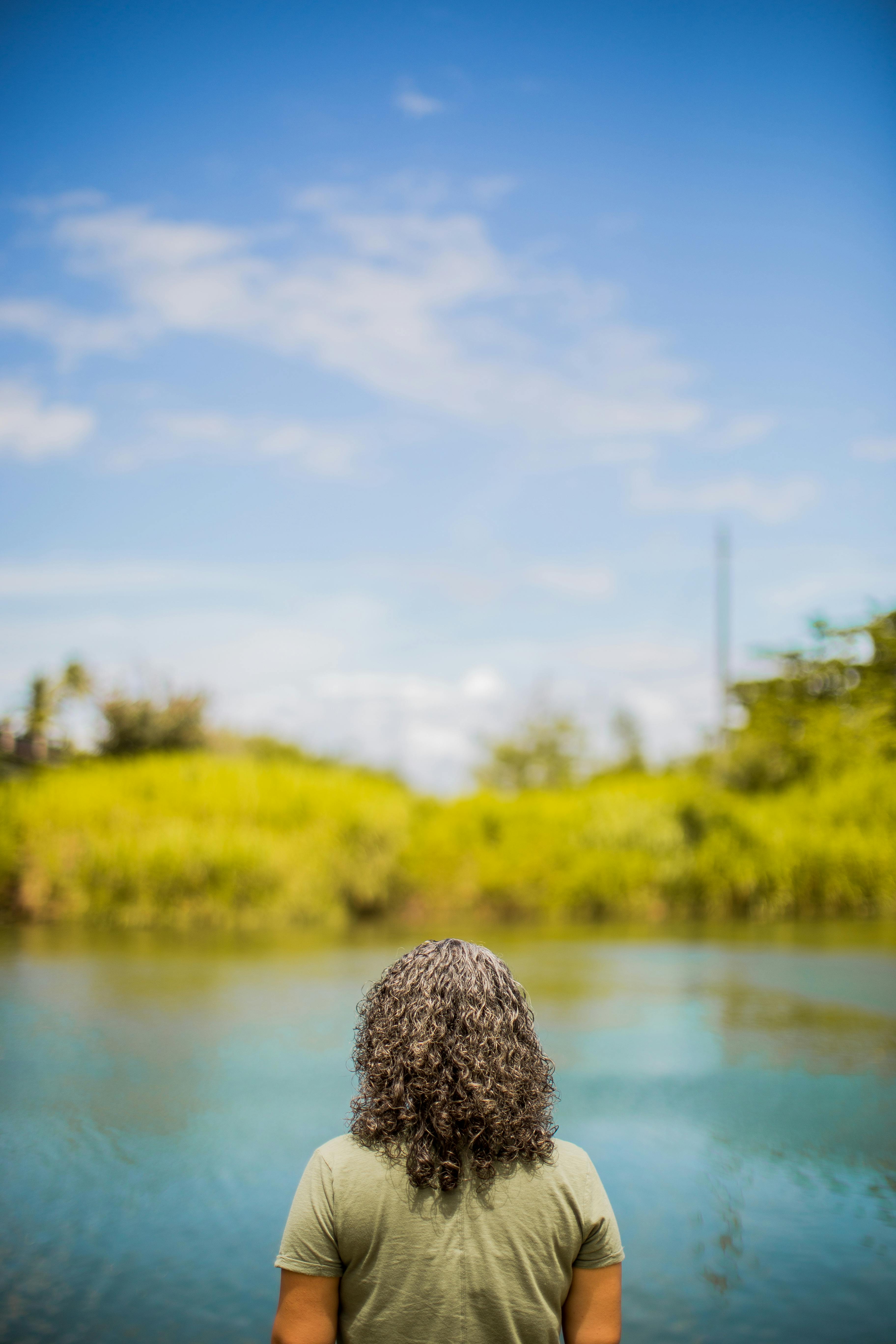 清澈的蓝天下，一个人在平静的河边，享受着郁郁葱葱的绿色植物