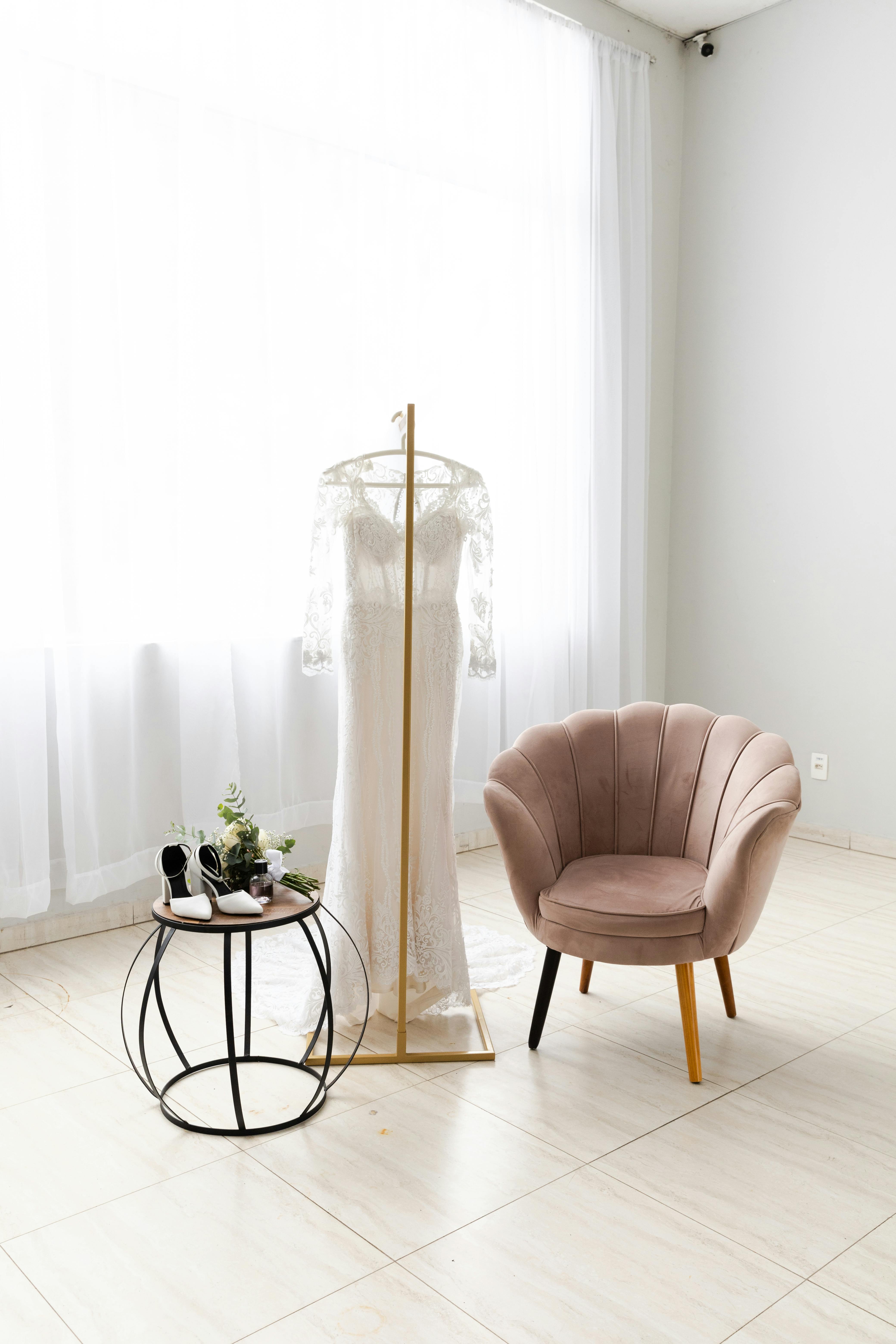 A beautifully detailed wedding dress on display with shoes and flowers in a modern interior.