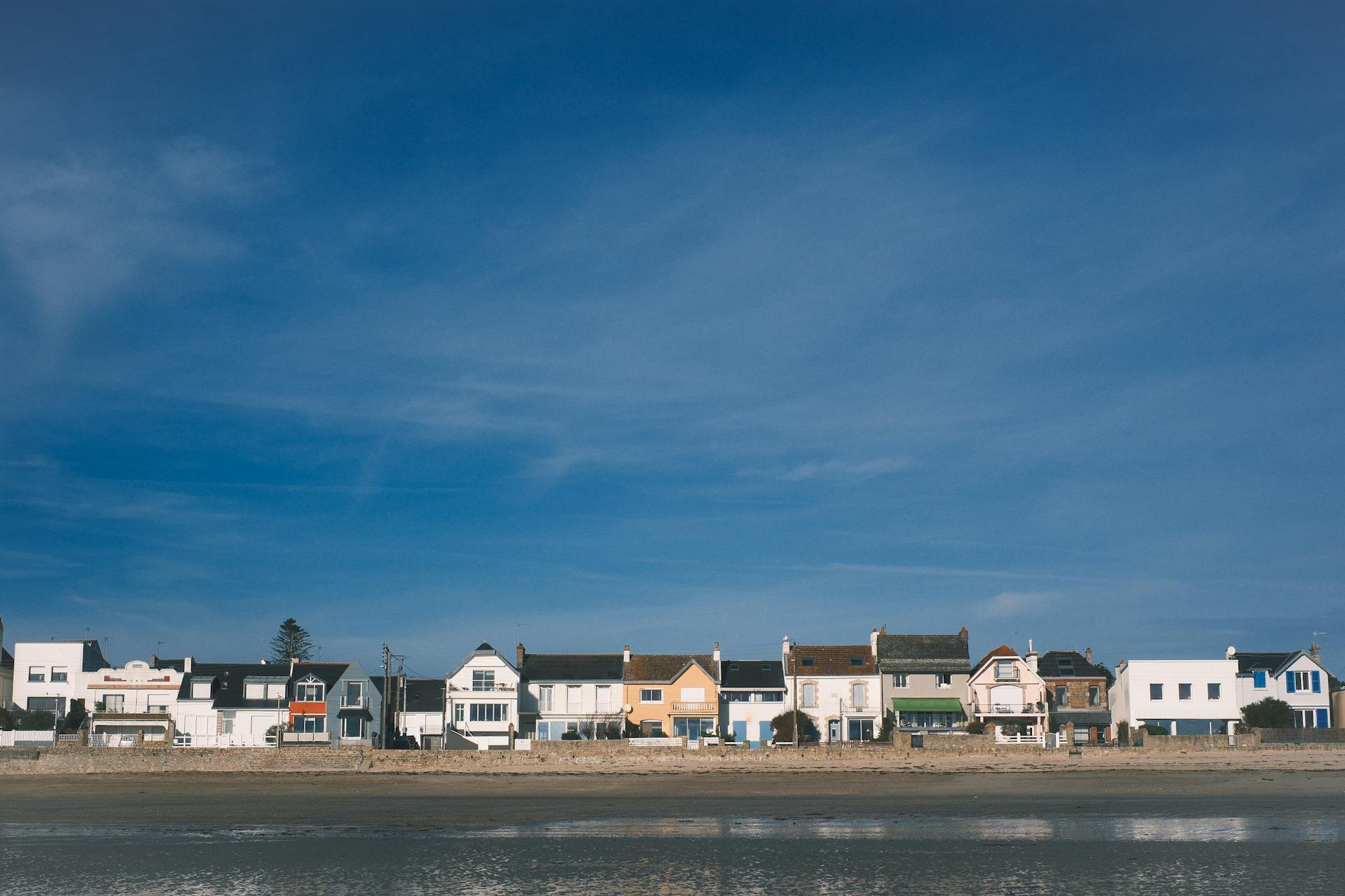 A row of colorful coastal homes by the sea with a blue sky backdrop.