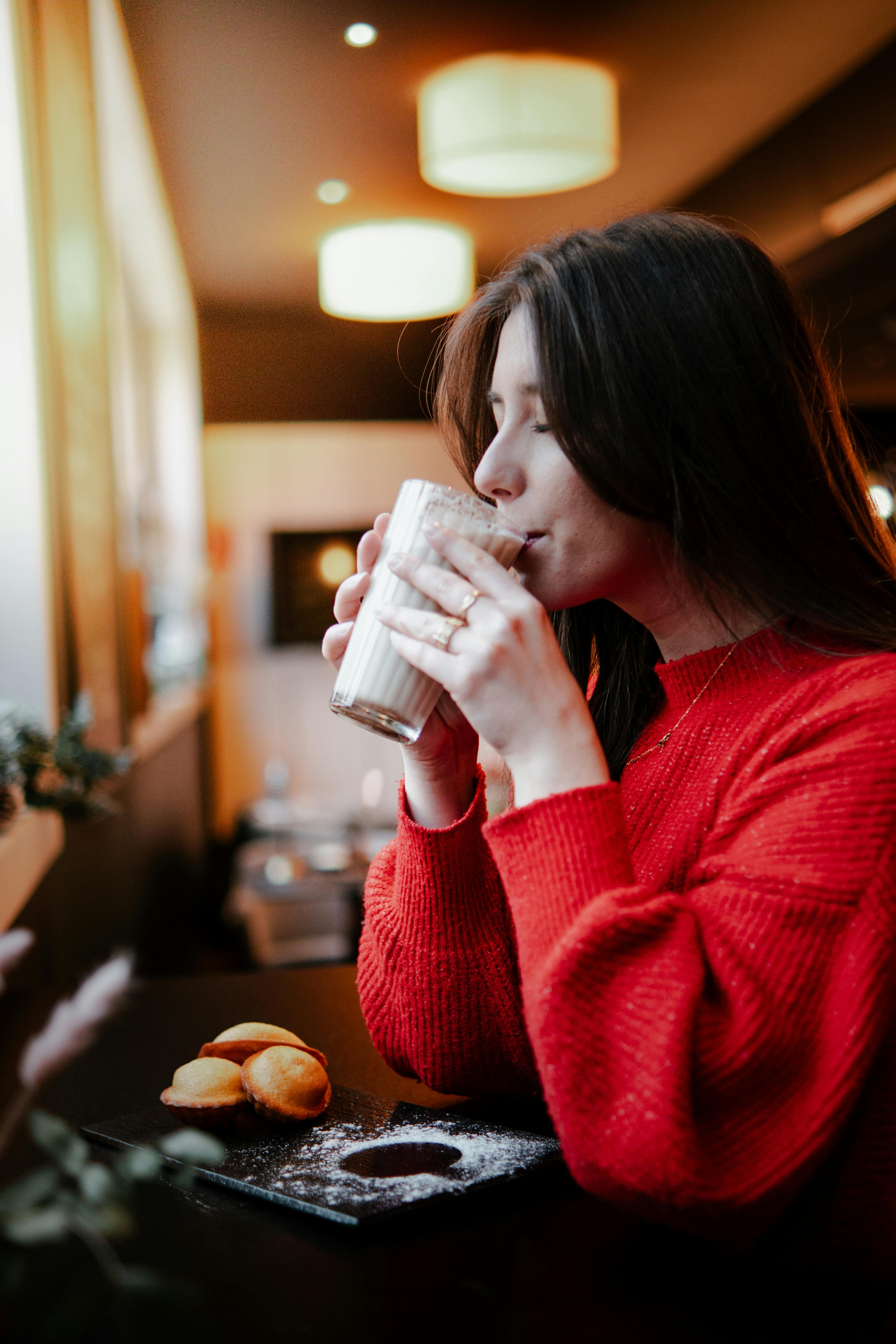 A woman in a red sweater savors a warm latte at a cozy café in Valenciennes, France.