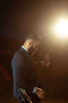 A sophisticated musician in a suit playing electric guitar under stage lights.