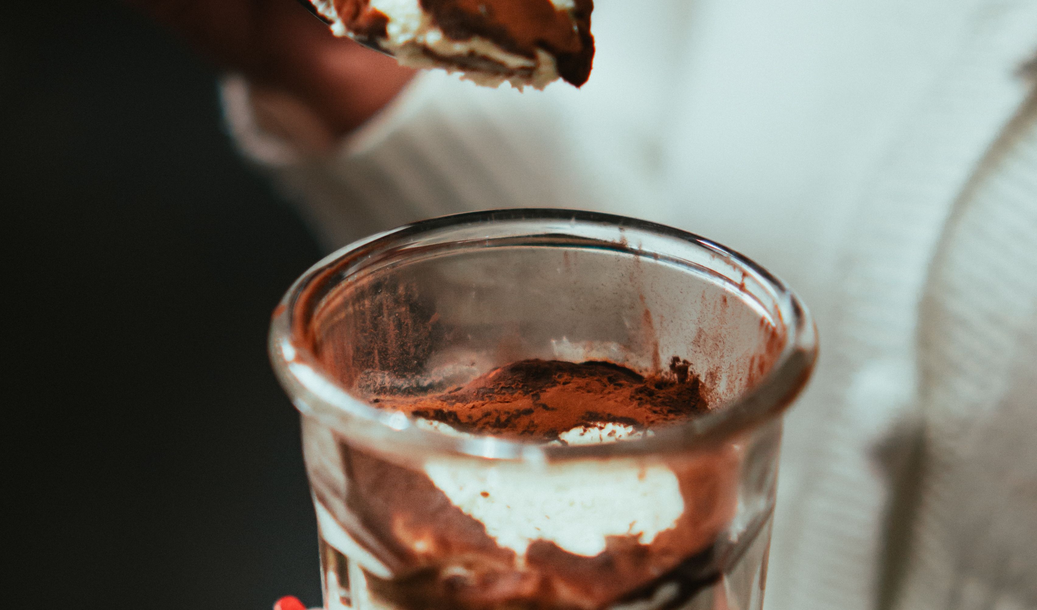 Tiramisu w szklance posypane kakao, łyżeczka nabiera krem