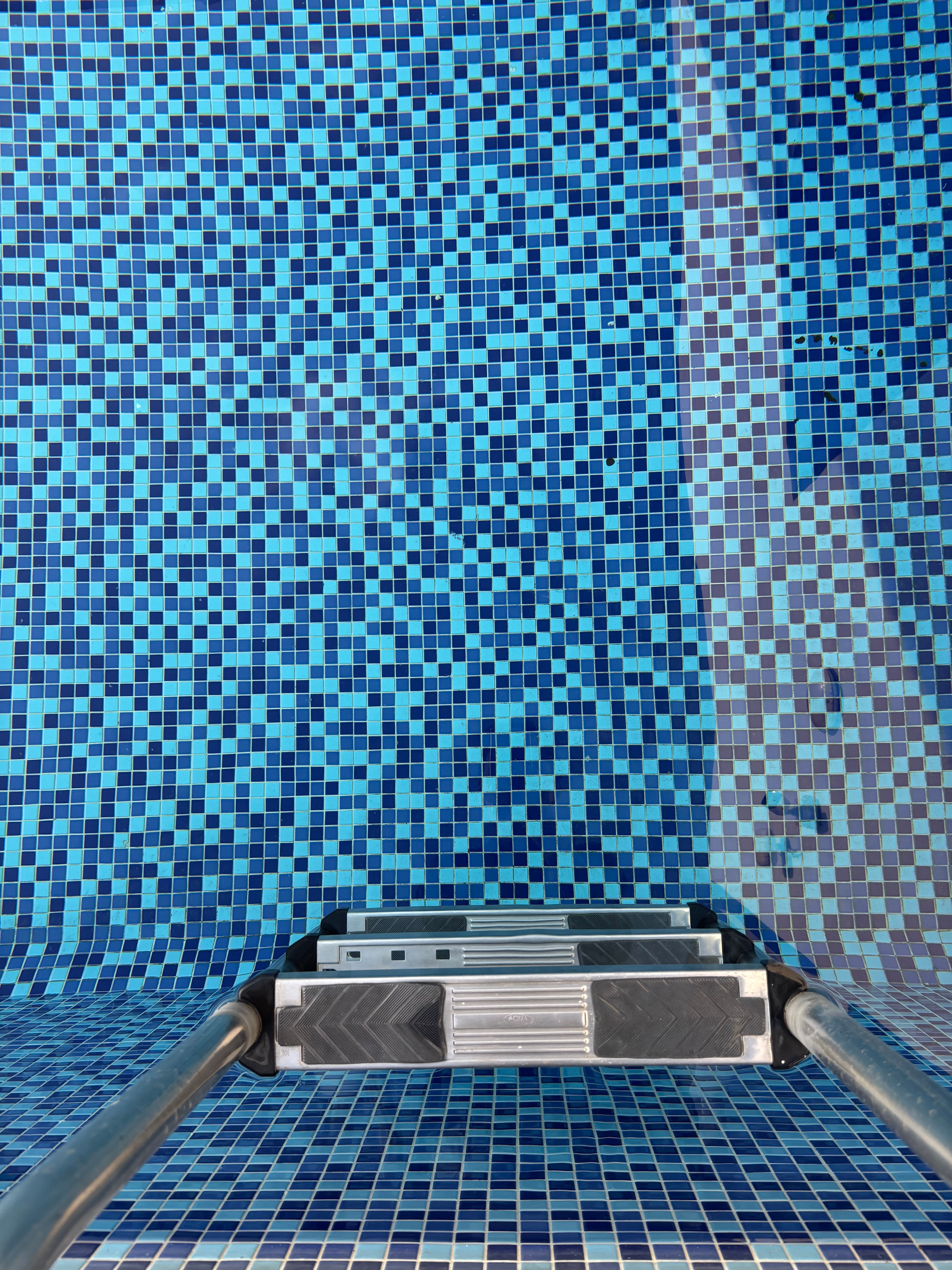 A dynamic perspective of a swimming pool featuring a vibrant blue mosaic tile pattern with ladder.
