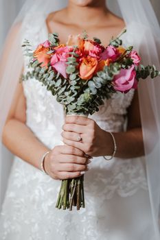Close-up of a bride holding a vibrant bouquet with pink and orange flowers, highlighting wedding elegance.