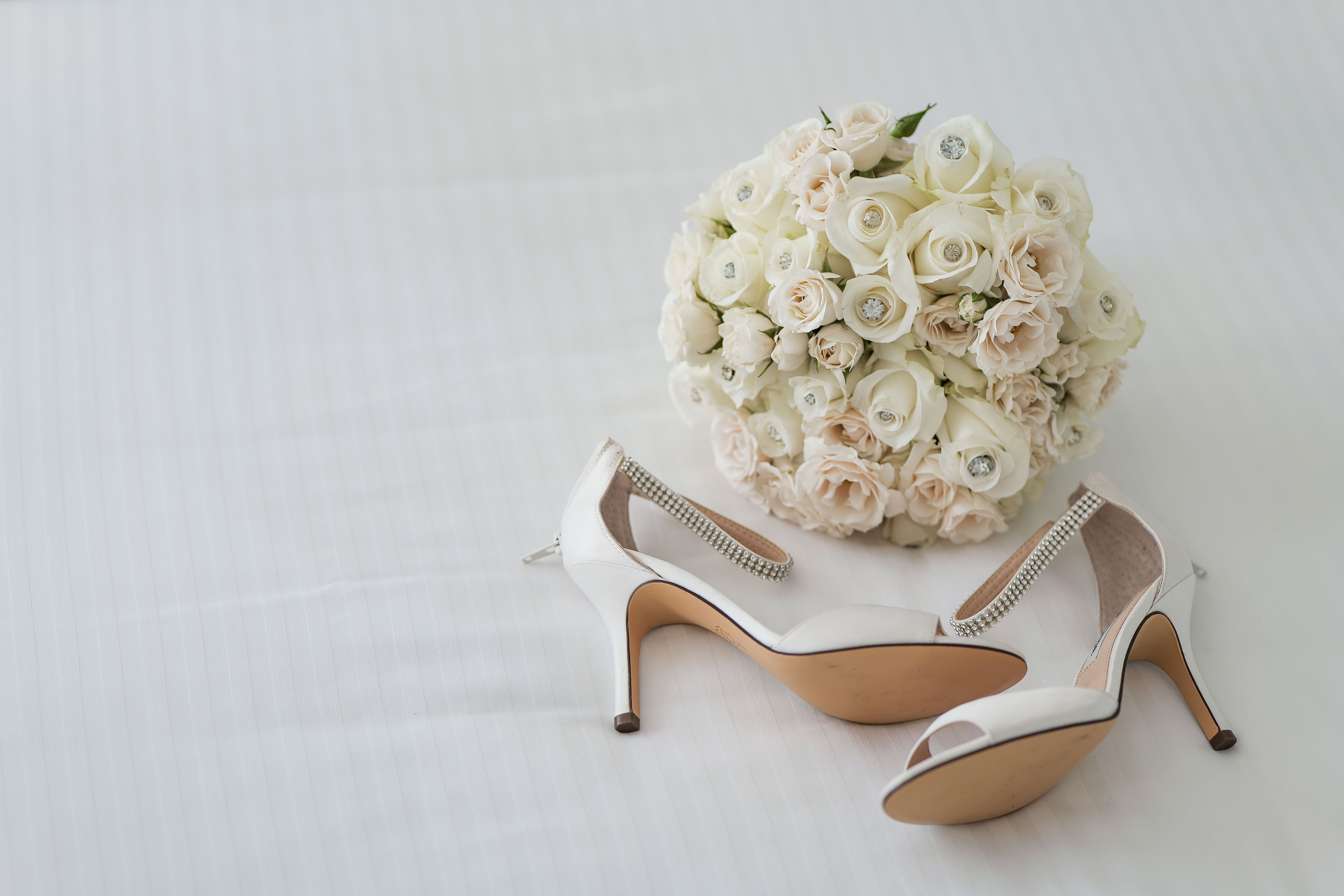 A beautiful arrangement of white high heels with a bouquet of white roses on a soft background.
